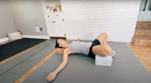 Fitness trainer lying in a rebound butterfly pose with yoga blocks supporting her knees and arms out long to her sides.