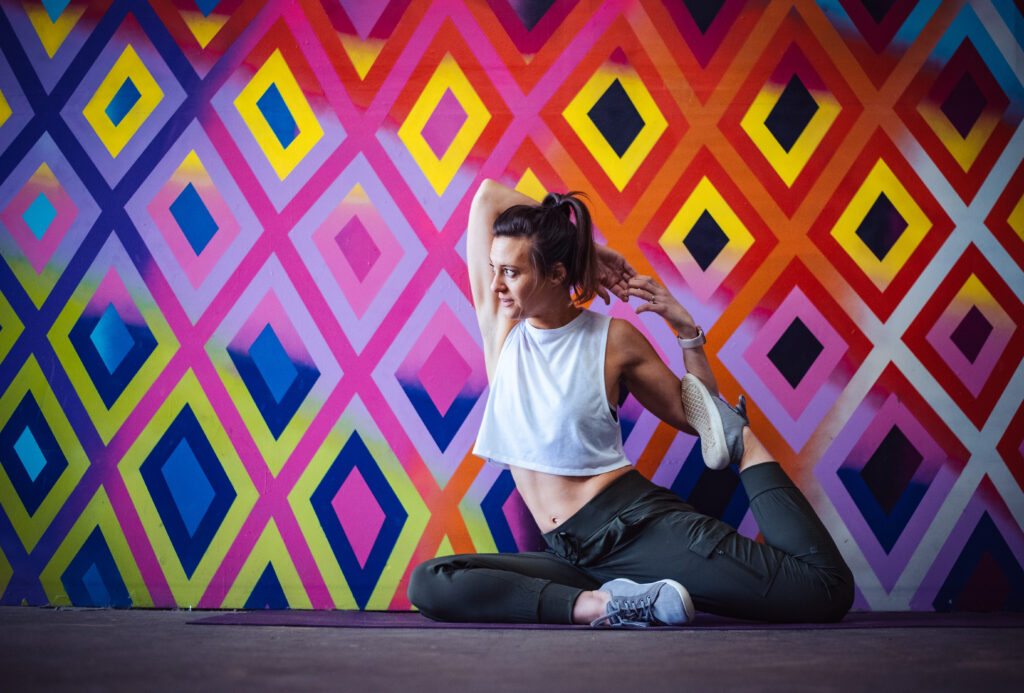 Fitness trainer doing mermaid pose against colorful diamond painted wall
