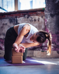 Fitness trainer stretching her arms using a yoga block.