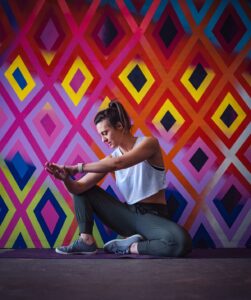 Fitness Coach performing a shoulder stretch in front of an artsy background.
